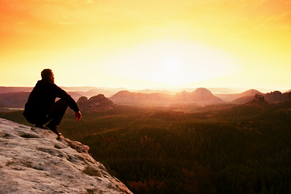 Young hiker in black and shirt is sitting on cliff's edge and enjoying spring morning in nature. Thinking about email privacy with sender control.